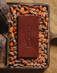 Tablette de chocolat noir Origines Chocolate Makers 70 % de cacao provenant du Liberia, entourée de fèves de cacao et de cabosses sur un fond en toile de jute.