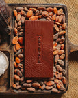 Tablette de chocolat noir à la fleur de sel du bassin d'Arcachon Origines Chocolate Makers, 70 % de cacao provenant du Pérou, entourée de fèves de cacao, de cabosses et d'un bol contenant du sel sur un fond en toile de jute.