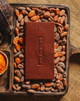 Tablette de chocolat noir au piment d'Espelette Origines Chocolate Makers 70 % de cacao provenant du Pérou, entourée de fèves de cacao, de cabosses et d'un bol contenant du piment d'Espelette sur un fond en toile de jute.