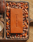 Tablette de chocolat au lait Origines Chocolate Makers 55 % de cacao provenant de Madagascar, entourée de fèves de cacao, de cabosses et d'un bol contenant du lait sur un fond en toile de jute.
