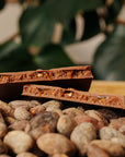 Tablette de chocolat fourrée aux cacahuètes sur un fond de fèves de cacao.