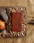 Tablette de chocolat noir Origines Chocolate Makers 70 % de cacao provenant de la coopérative Cabruca à Bahia, Brésil, entourée de fèves de cacao et de cabosses sur un fond en toile de jute.
