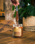 Pot de pâte à tartiner bio noisettes romaines et chocolat d'Origines Chocolate Makers, avec une cuillère soulevant la pâte, sur une table en bois dans un cadre chaleureux.