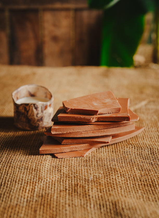 Morceaux de chocolat au lait empilés avec un bol de lait sur une toile de jute, en arrière-plan naturel.