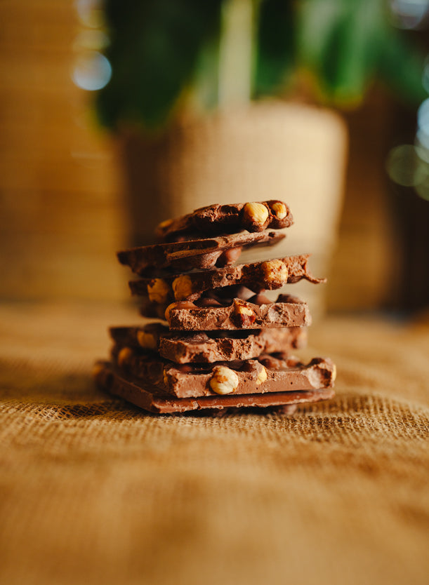 Morceaux de chocolat au lait aux noisettes empilés sur une toile de jute, en arrière-plan naturel.
