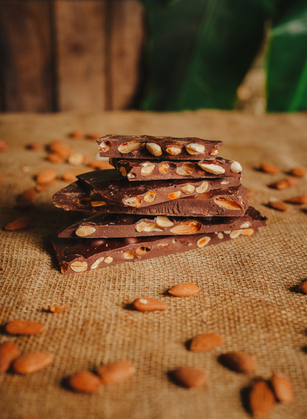 Morceaux de chocolat noir aux amandes empilés sur une toile de jute, avec des amandes dispersées autour, en arrière-plan naturel.