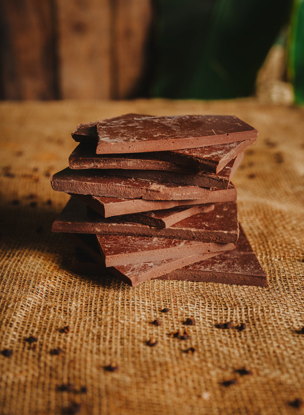 Morceaux de chocolat noir au poivre de Timut empilés sur une toile de jute, avec du poivre dispersé autour, en arrière-plan naturel.