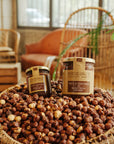 Pots de pâte à tartiner bio noisettes romaines et chocolat d'Origines Chocolate Makers dans un panier contenant des noisettes dans un cadre chaleureux.